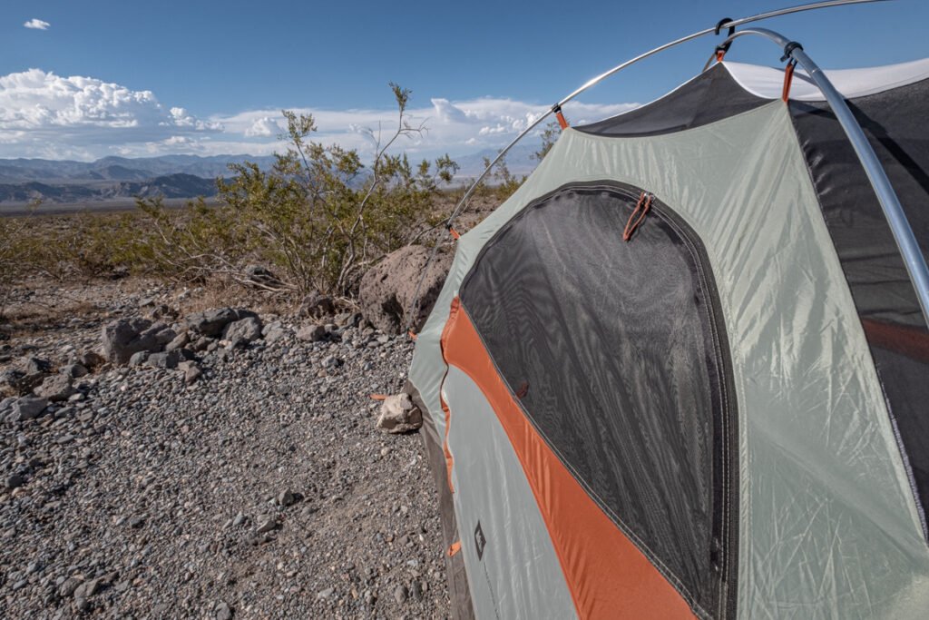 A sage green tent with orange trim pitched in the desert with a blue sky in the background.