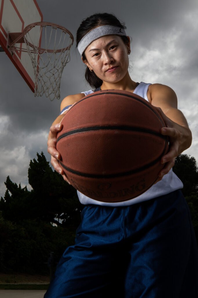 A woman holds a basketball towards the camera with a serious expression on her face.