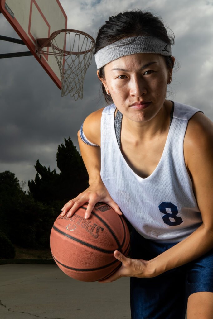 A woman holds a basketball away from the camera with a serious expression on her face.