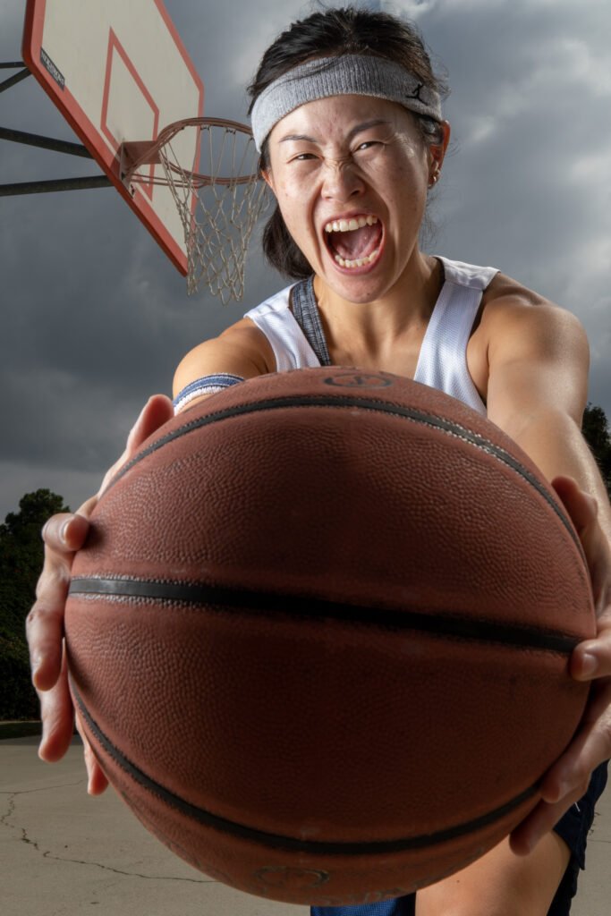 A woman holds a basketball towards the camera while looking like she is screaming.