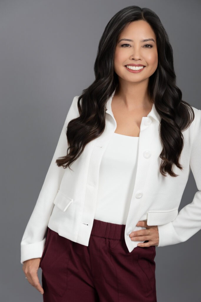 A woman wearing a white top leans against a wall.